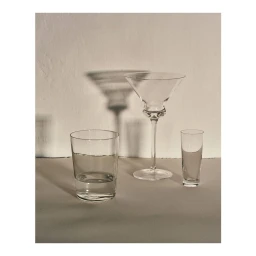 Three empty glass vessels casting sharp shadows on a plain wall and surface captured in New York by Rich Stapleton.