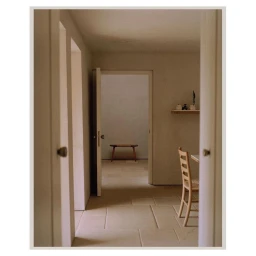 Interior architectural view through a doorway showing a wooden bench, stone tiled floor, and neutral walls captured by Rich Stapleton.