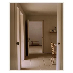Minimalist interior view through doorways showing a wooden chair and bench in a neutral-toned room by Rich Stapleton