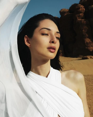 Close up portrait of a woman in a white halter top holding a sheer white fabric against a rocky desert landscape