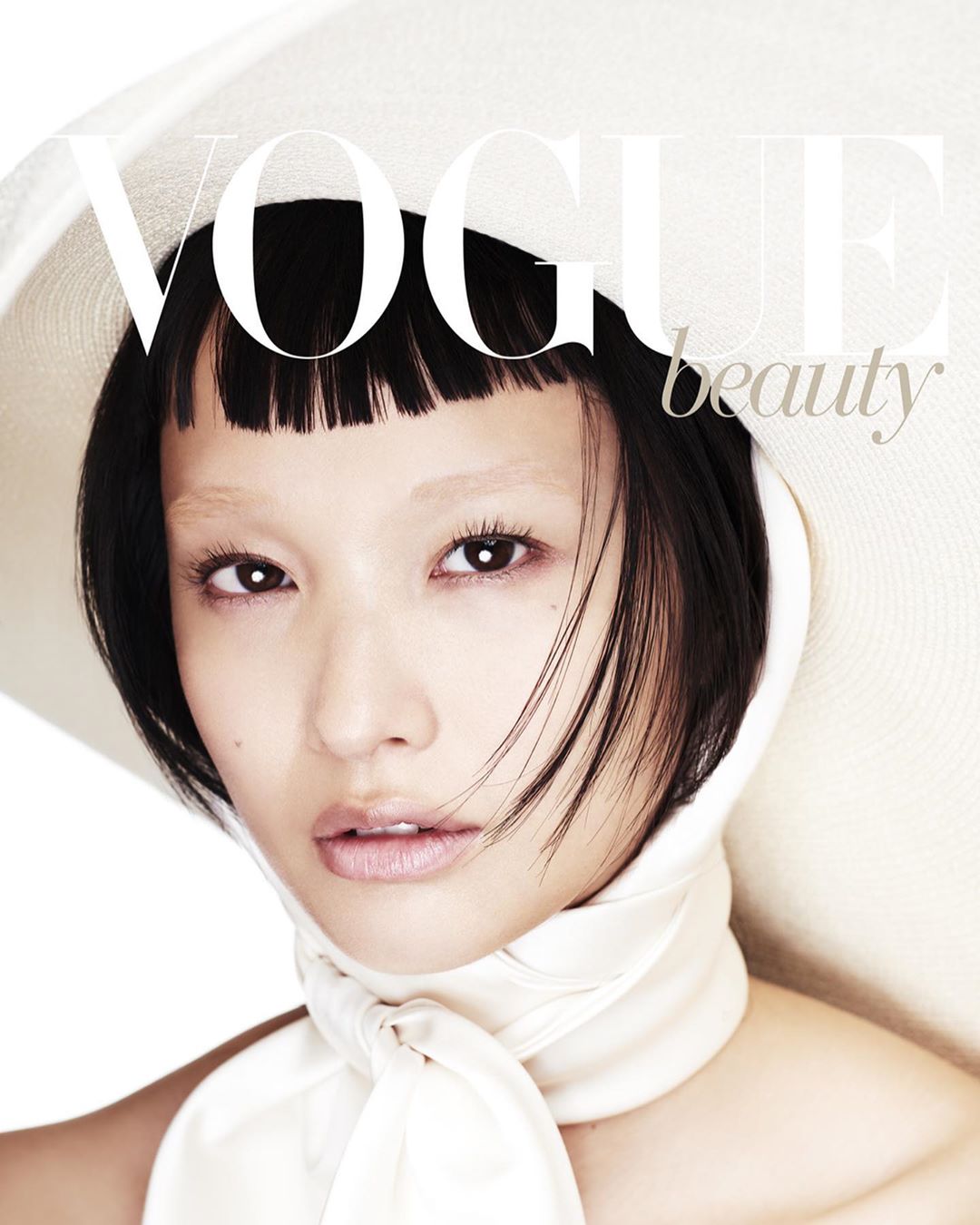 Asian woman with a white hat on the cover of Vogue Beauty magazine, close-up portrait, fashion and beauty editorial shot.