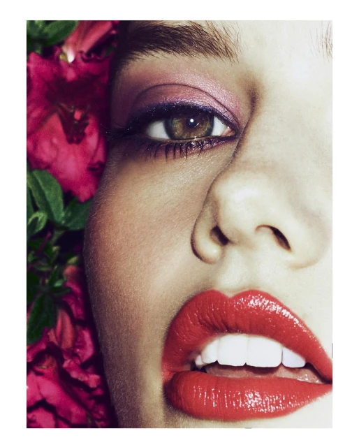 Close-up of a woman's face with vivid makeup, highlighting her red lipstick, pink eyeshadow, and the lush pink flowers framing her.