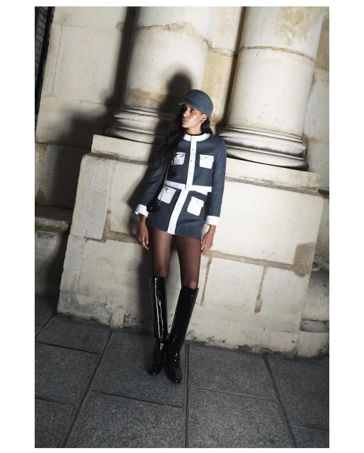 Elegant woman in a short blue and white dress with matching hat posing near stone columns in shiny black boots. Fashion photography.