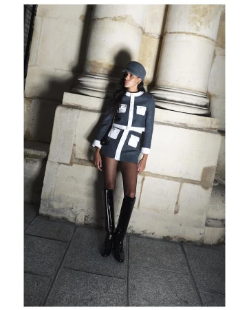 Elegant woman in a short blue and white dress with matching hat posing near stone columns in shiny black boots. Fashion photography.