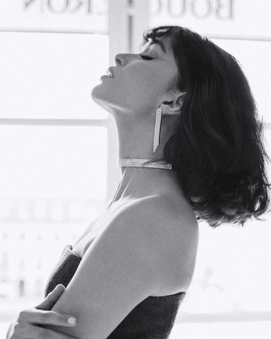 Black and white portrait of a woman with dark hair wearing a choker and pendant earrings with head tilted back