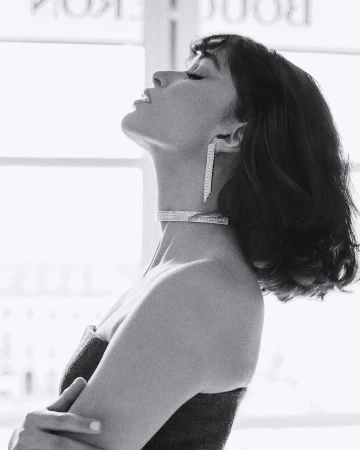 Black and white portrait of a woman with dark hair wearing a choker and pendant earrings with head tilted back