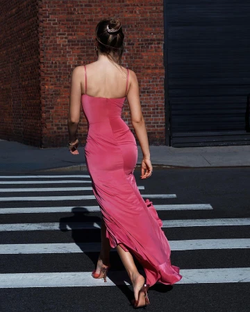 Woman walking away on a street wearing a long pink slip dress and clear heeled sandals.