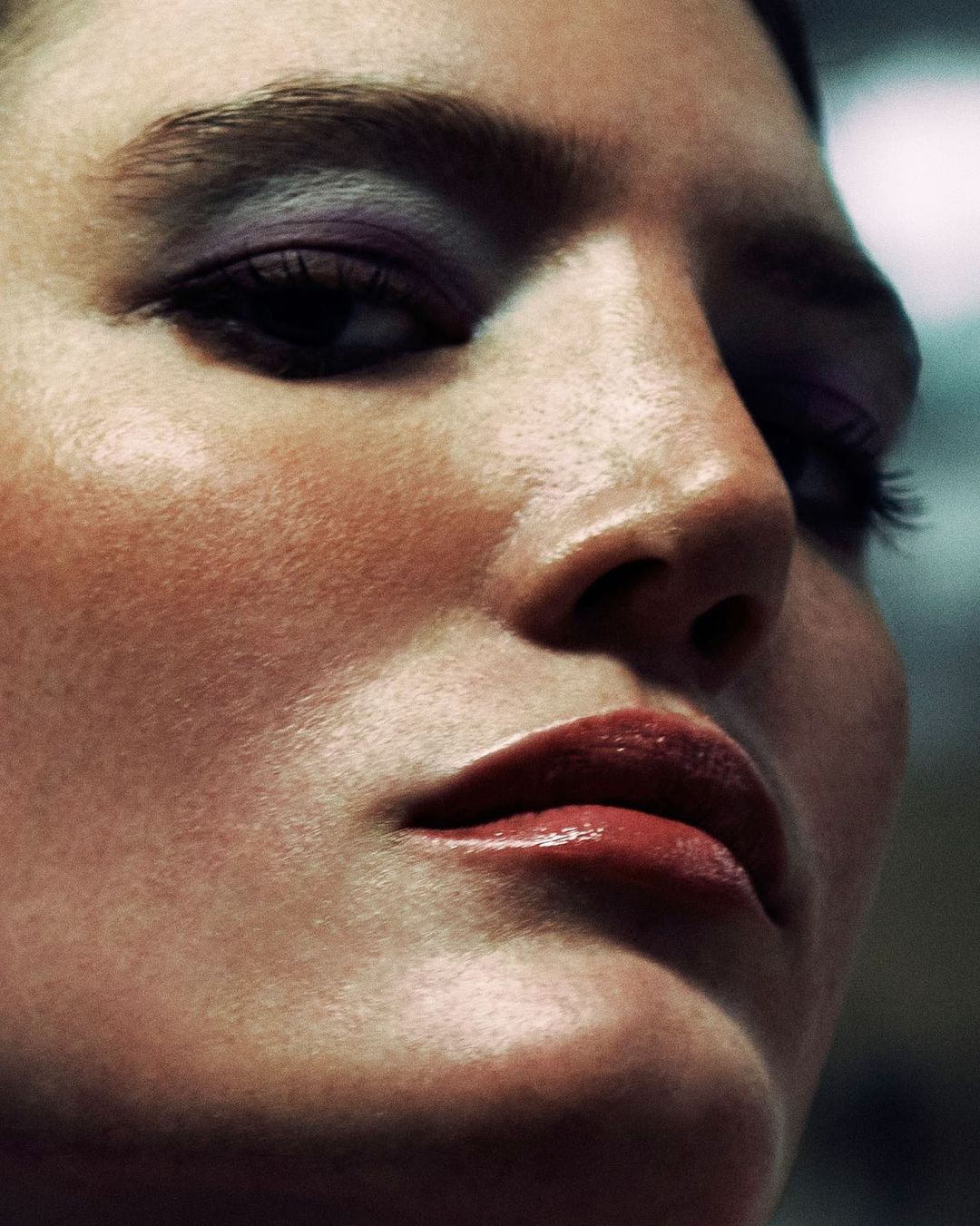 Close-up portrait of a woman with dramatic purple eyeshadow and glossy lips photographed by Rayan Ayash.