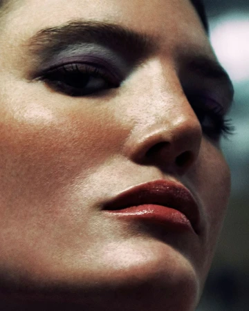 Close-up portrait of a woman with dramatic purple eyeshadow and glossy lips photographed by Rayan Ayash.