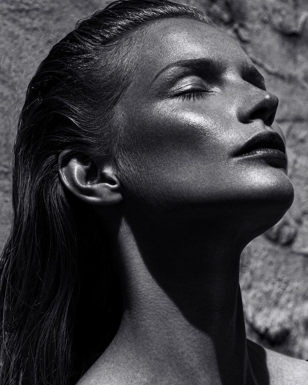Monochrome portrait of a woman with wet hair tilted back and eyes closed under harsh directional sunlight by Rayan Ayash
