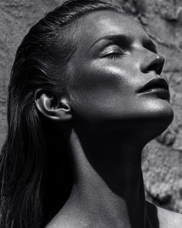 Monochrome portrait of a woman with wet hair tilted back and eyes closed under harsh directional sunlight by Rayan Ayash