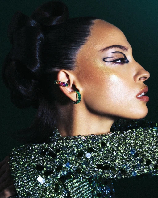 Profile of a stylish woman with dark hair, dramatic black eyeliner, and gemstone earrings, wearing a green sequined top.