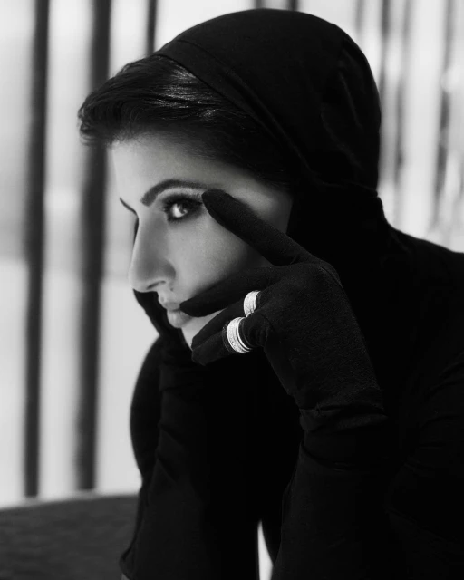 Striking black and white portrait of an adult female with stylish makeup wearing a headscarf, gloves, and rings in an indoor setting.