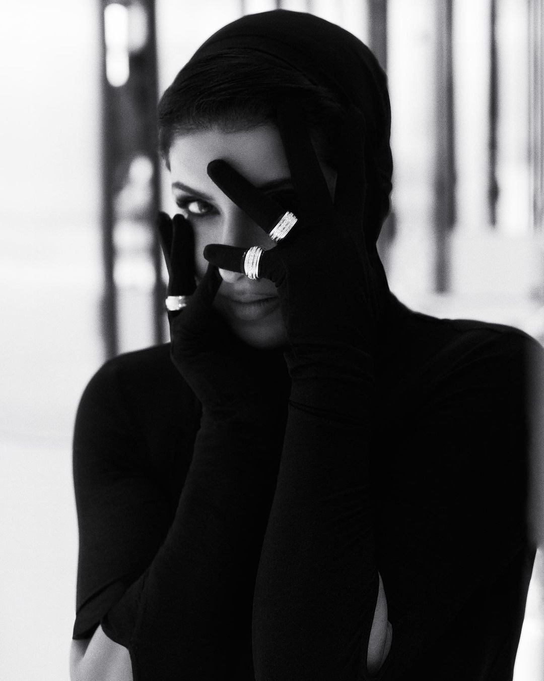 Black and white portrait of a woman wearing black gloves and rings while partially covering her face with her hands.