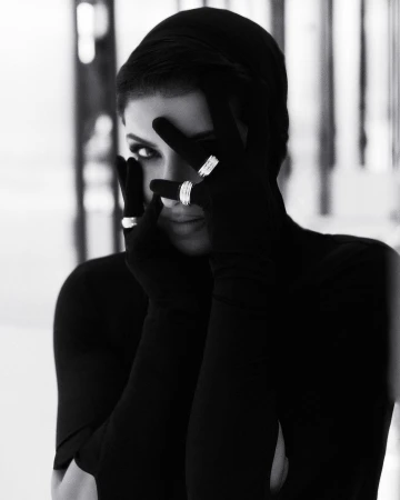 Black and white portrait of a woman wearing black gloves and rings while partially covering her face with her hands.