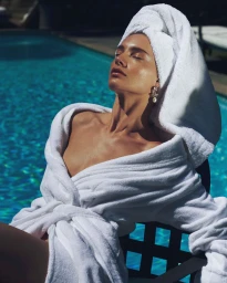 Woman in a white bathrobe and matching towel wrap relaxing poolside with eyes closed