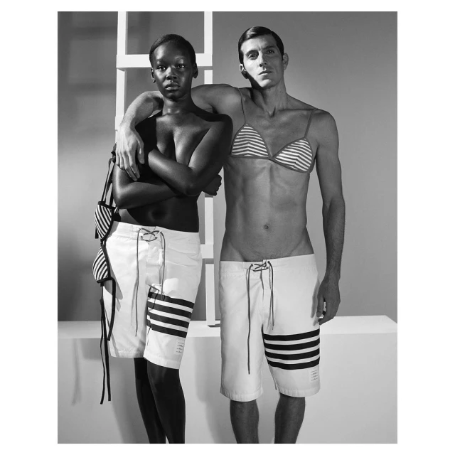 Black and white studio portrait of an African woman and Caucasian man wearing matching striped swimwear and white shorts.