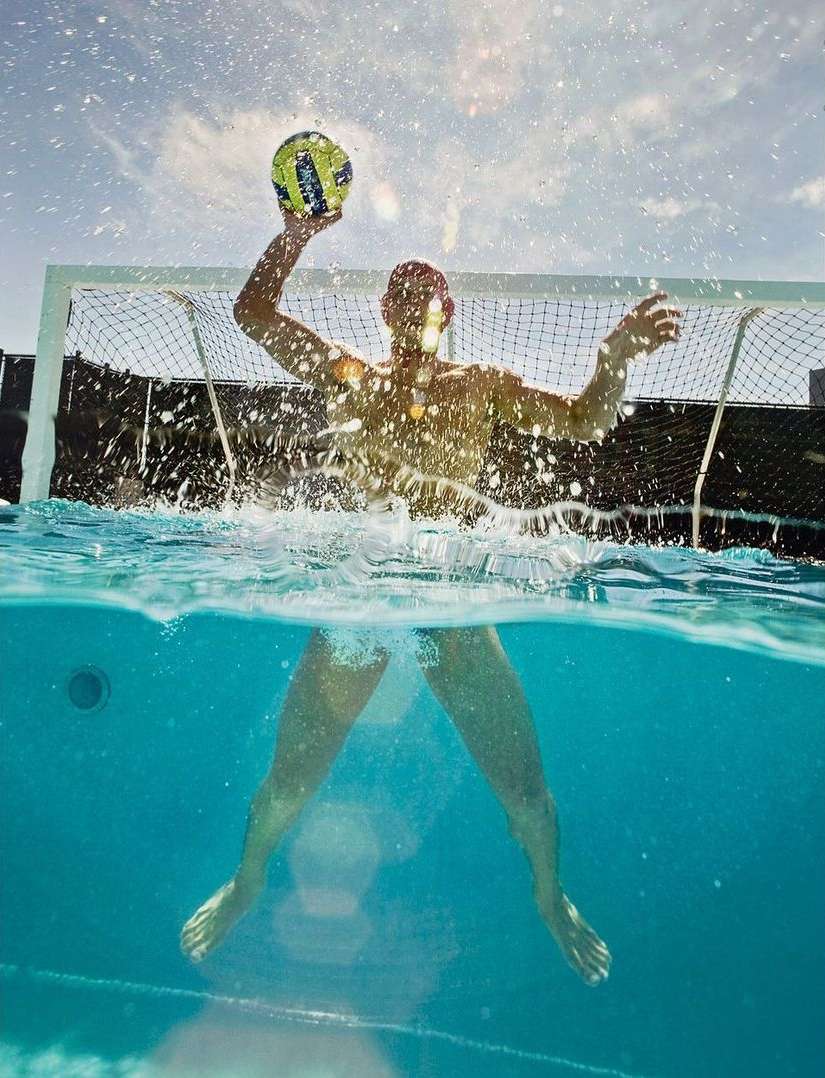 Water polo player in action, throwing the ball in a pool during a game, viewed from an underwater perspective. 