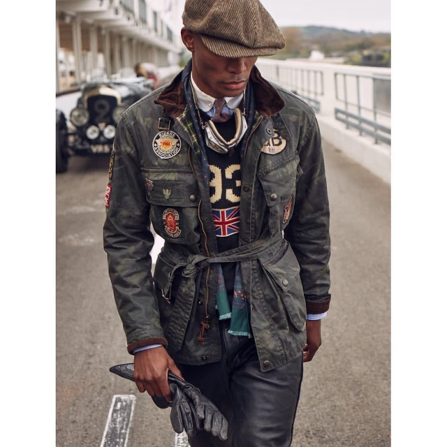 Stylish adult male model wears a vintage-inspired racing jacket, cap, and gloves, posing with a classic car in the background.