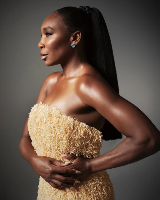 Portrait of Venus Williams in a textural strapless dress with slicked-back hair and blue earrings, posing in a studio with a gray background.