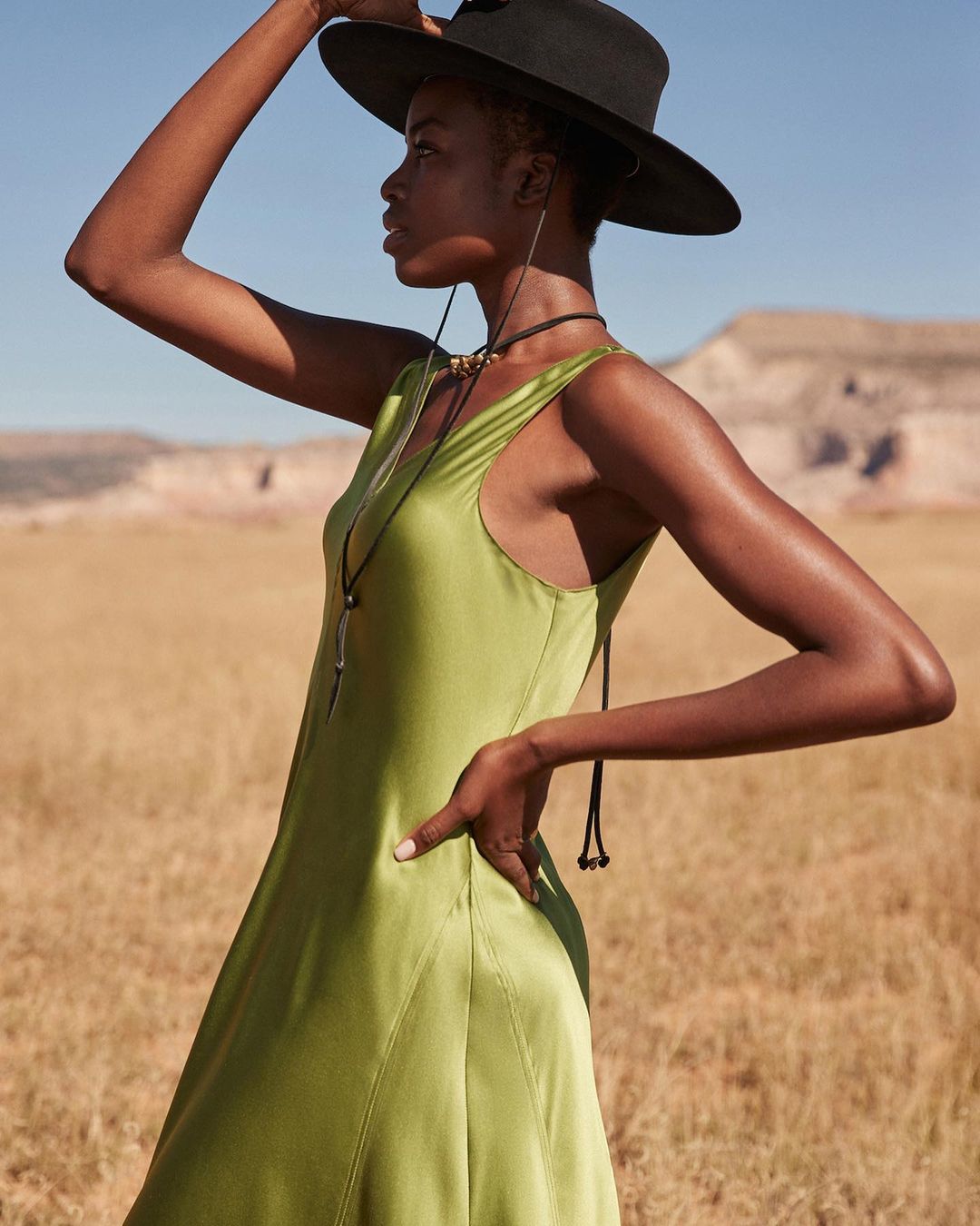 Black woman in a green silk dress and wide-brimmed hat posing in a desert landscape by Richard Phibbs.