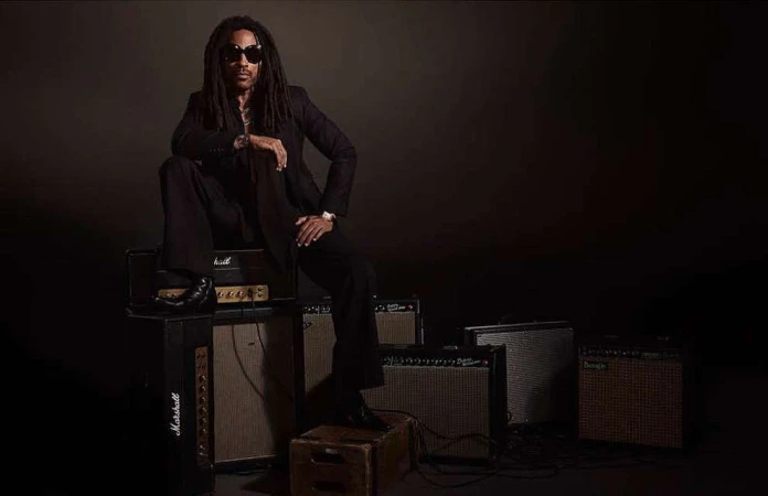 Portrait of a Black adult male wearing sunglasses and a suit, seated on a stack of Marshall amplifiers in a photo studio setting.