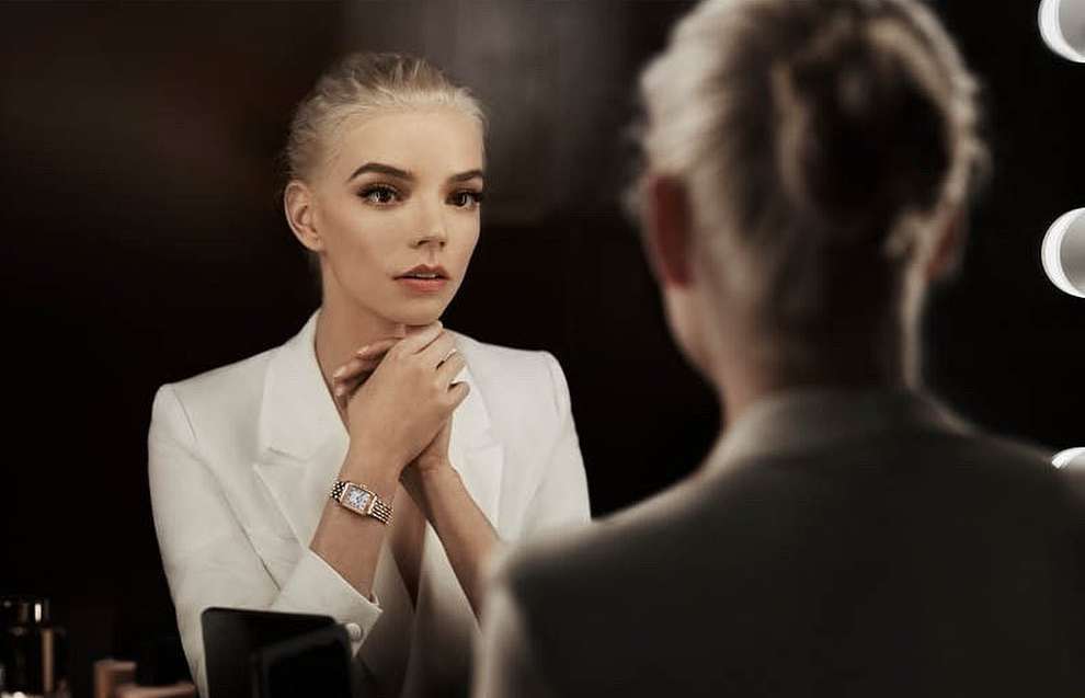 Blonde woman in white suit looks in a mirror in an indoor setting. The face of the reflection is out of focus.