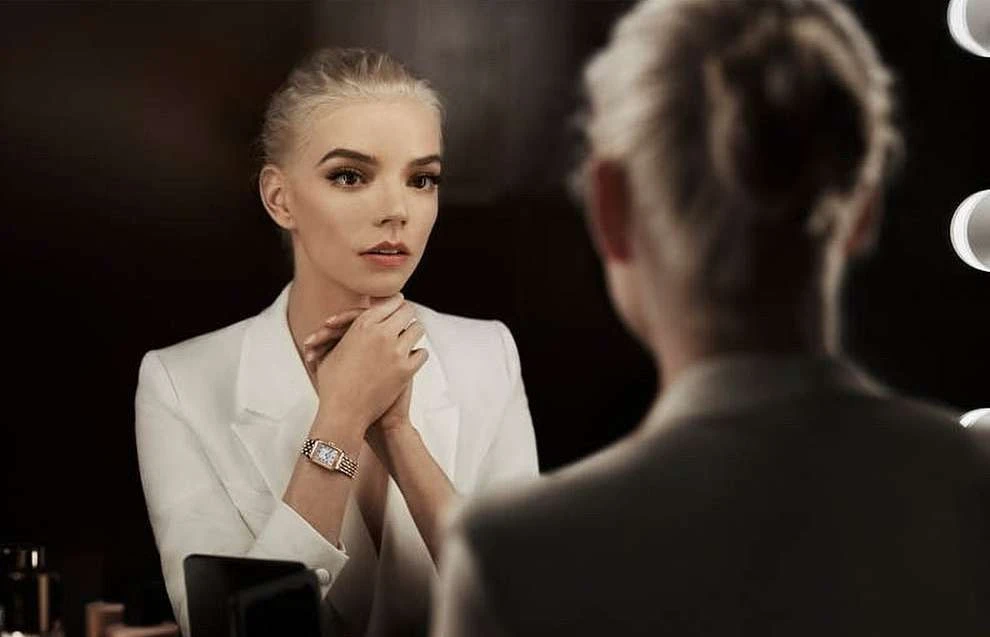 Blonde woman in white suit looks in a mirror in an indoor setting. The face of the reflection is out of focus.