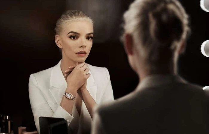 Blonde woman in white suit looks in a mirror in an indoor setting. The face of the reflection is out of focus.