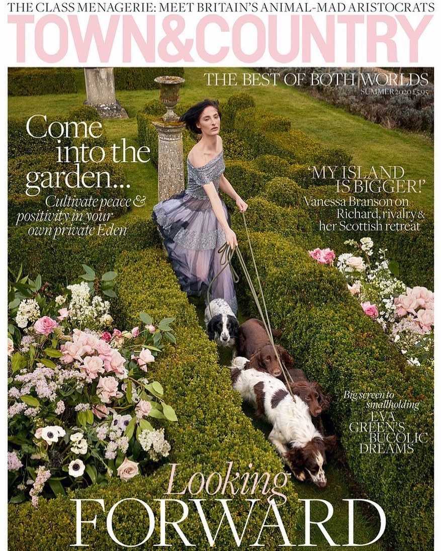 Magazine cover of woman in gown walking dogs through garden path, surrounded by greenery and flowers, featuring the title Town & Country.