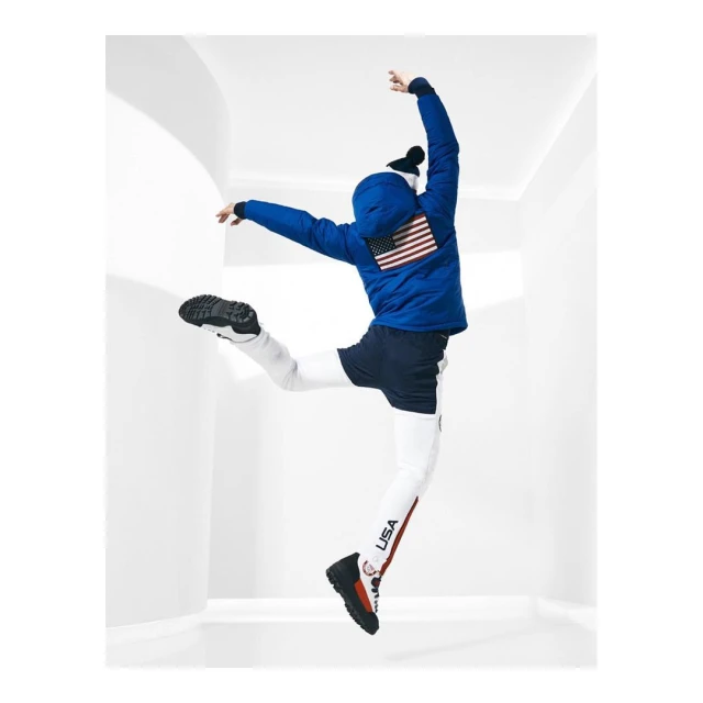 Person in mid-air wearing a blue USA flag winter coat, leggings with 'USA' printed on the side, and black beanie and sneakers.
