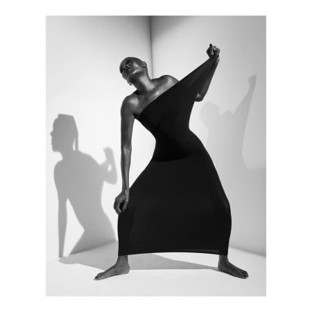 Black and white portrait of a bald woman in a black dress stretching the fabric against a plain studio background.