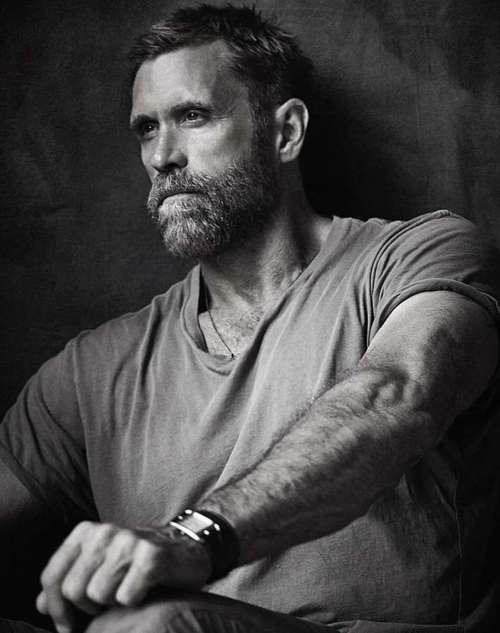 Monochrome portrait of a bearded man in his 40s wearing a t-shirt against a dark textured backdrop