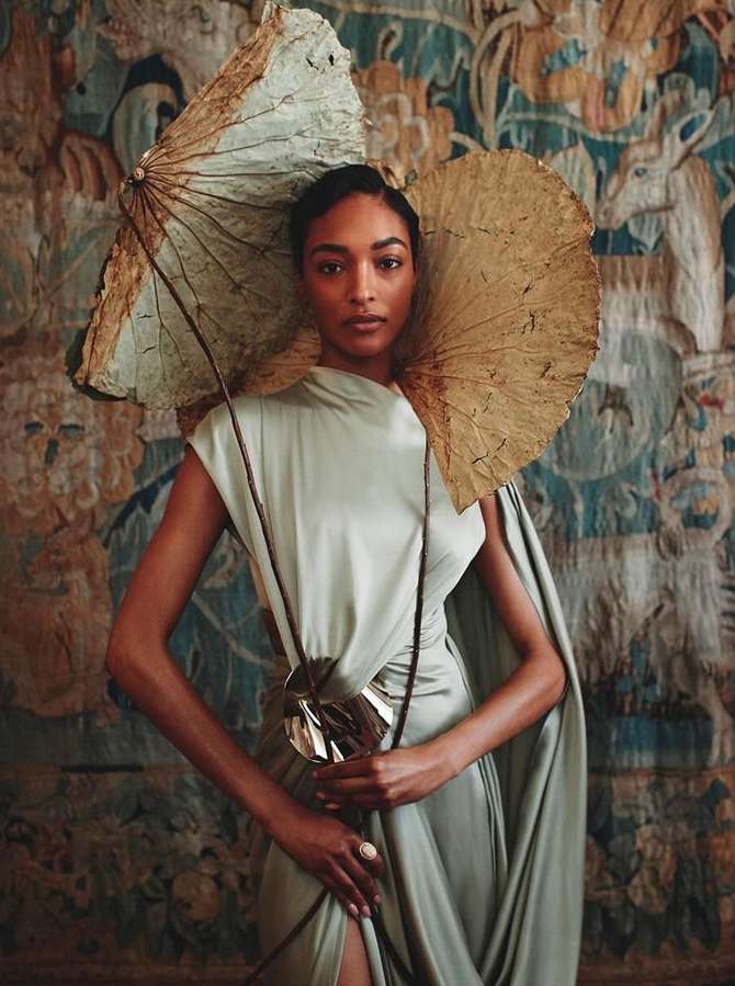 Elegant studio portrait of an African American woman in a flowing pale green gown, adorned with a large dried lotus headdress and statement ring.