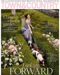 Woman in an off-the-shoulder patterned dress walking four dogs on leashes through a manicured topiary garden.