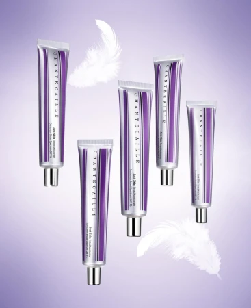 Chantecaille skincare product tubes displayed with white feathers against a soft gradient purple background in a beauty product shot.