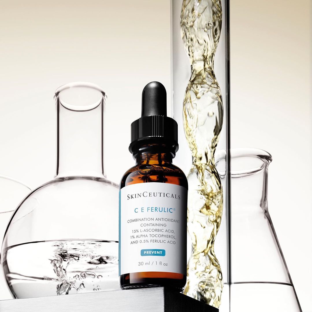 Skinceuticals C E Ferulic bottle with dropper displayed with scientific glassware, including beakers and a test tube with clear liquid.