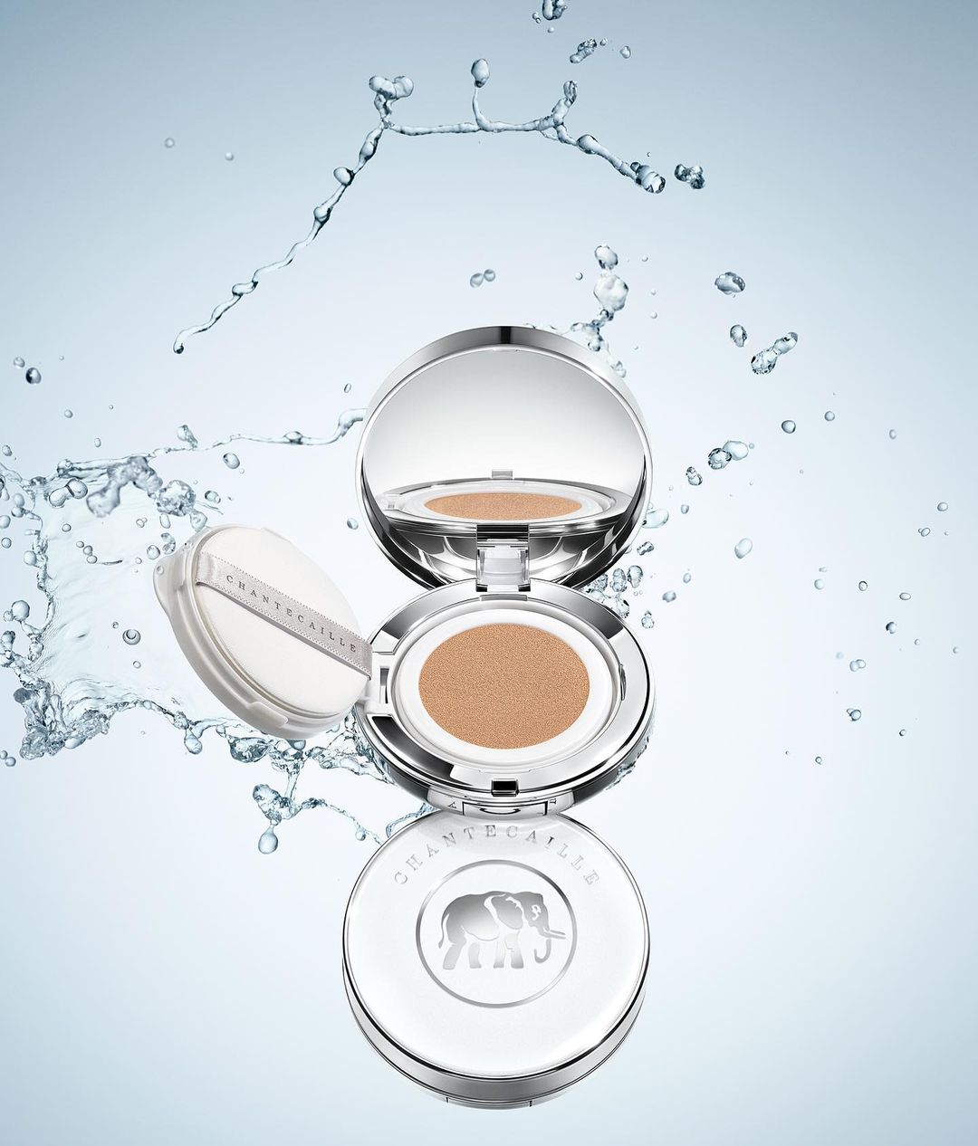 Chantecaille compacts floating in a blue and white space surrounded by water droplets in a beauty and product shot, luxury.