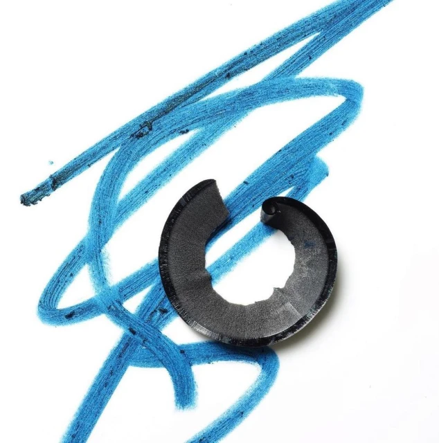 Close-up of a broken black cosmetic pencil sharpener shaving with bright blue cosmetic pencil markings on a white background.