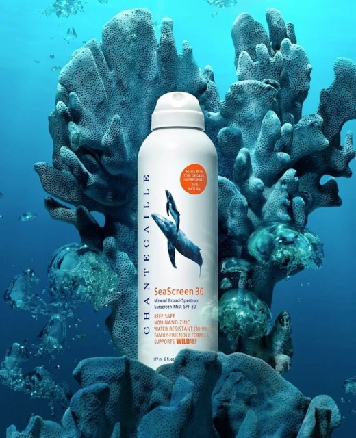 Chantecaille SeaScreen 30 sunscreen spray bottle with coral background in an underwater setting. Beauty shot with ocean feel.