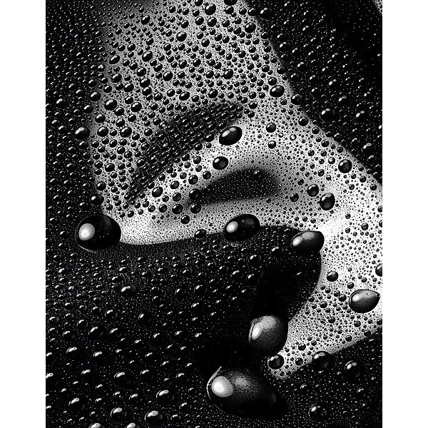 Close-up of water droplets on a black surface creating an abstract design with areas of foam and liquid texture.