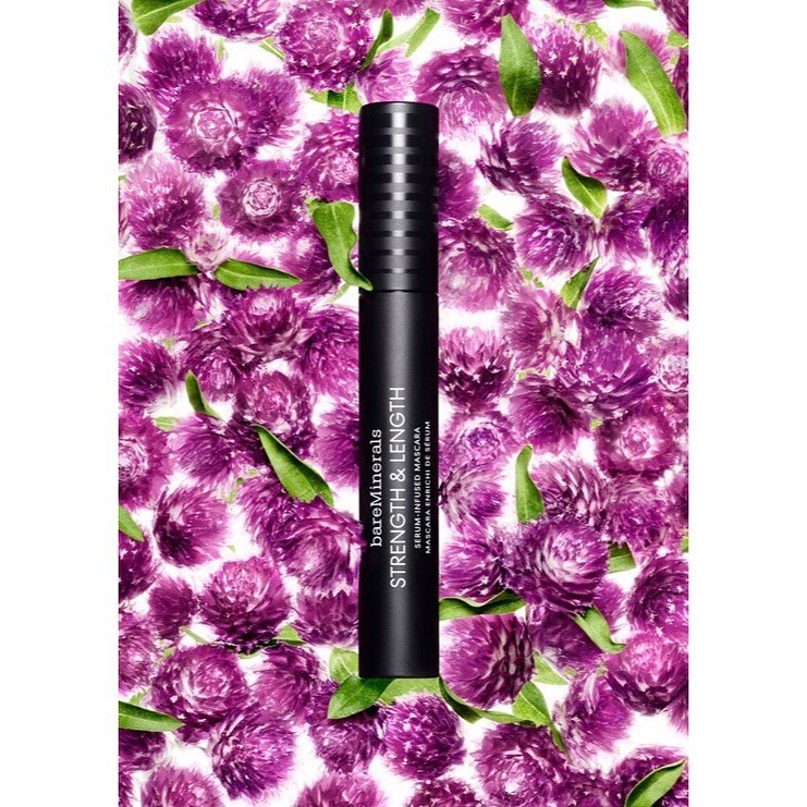 Close-up of bareMinerals mascara on a backdrop of purple globe amaranth flowers and green leaves, makeup and beauty concept.