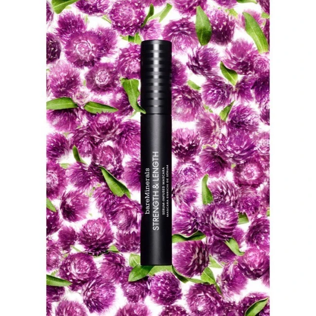 Close-up of bareMinerals mascara on a backdrop of purple globe amaranth flowers and green leaves, makeup and beauty concept.