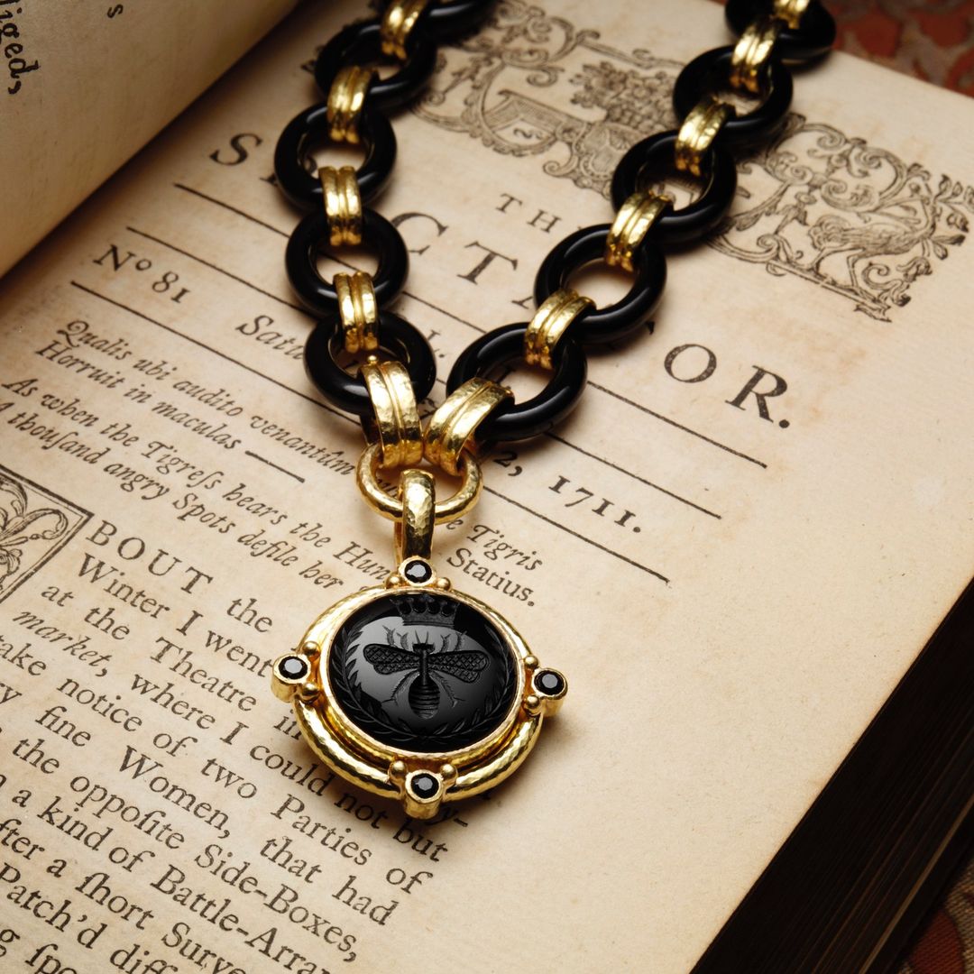 Gold and black necklace with a bee pendant displayed on an antique book page with faded text.