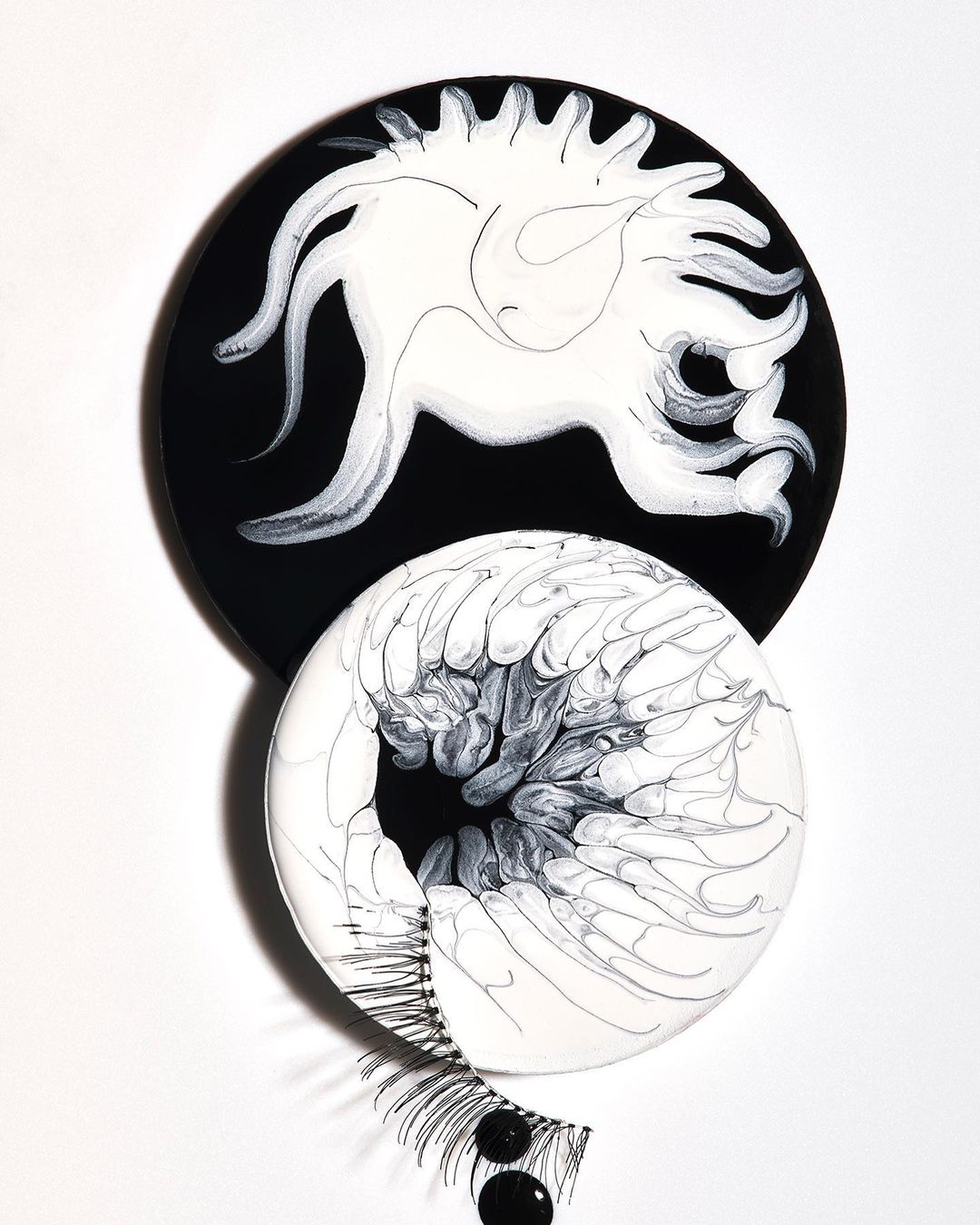 Abstract art featuring black and white circular forms with eyelash accents against a white backdrop. Minimalist aesthetic and design focus.