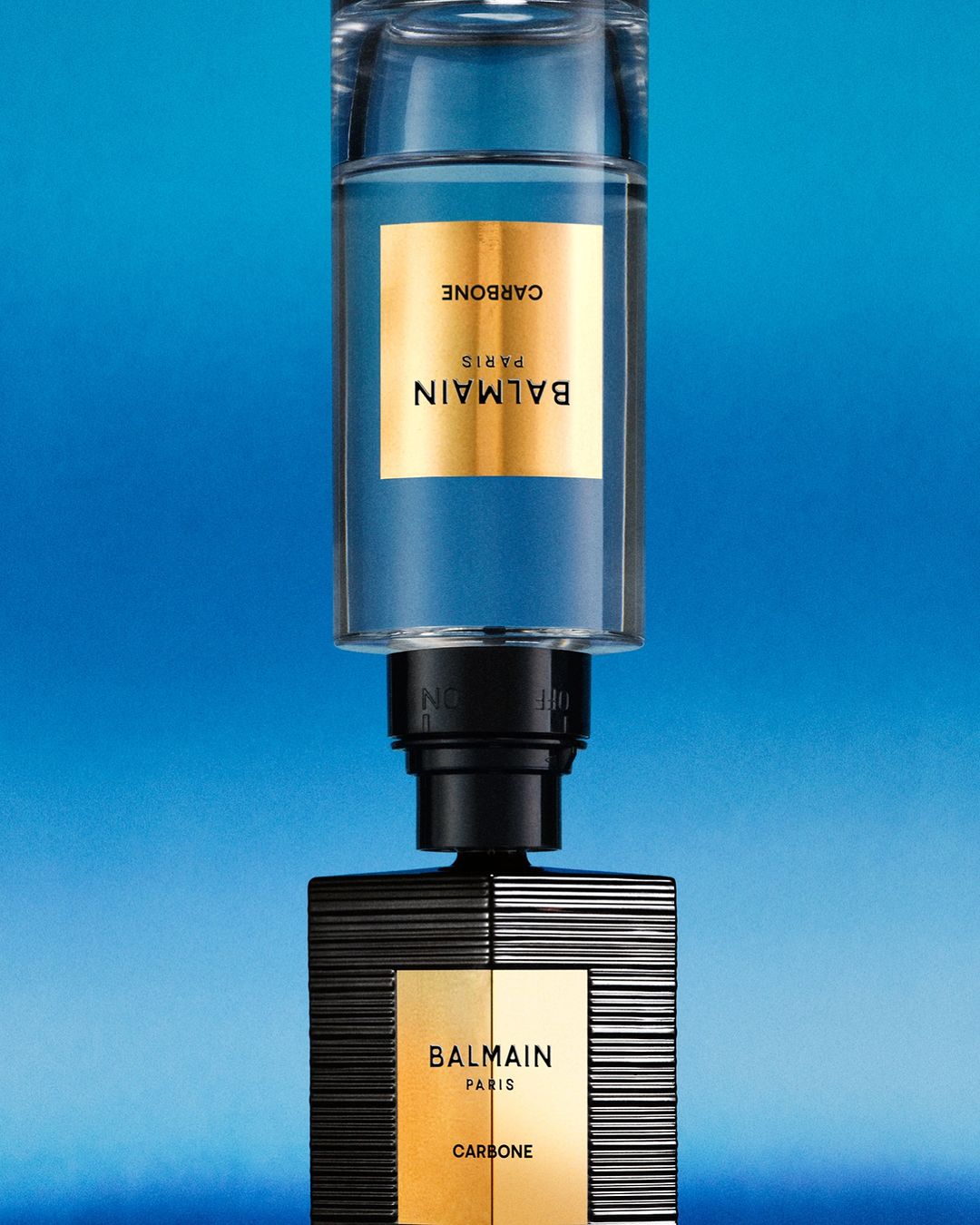 Two stacked Balmain Carbone perfume bottles are displayed against a vibrant blue background, emphasizing the brand's luxury and design.