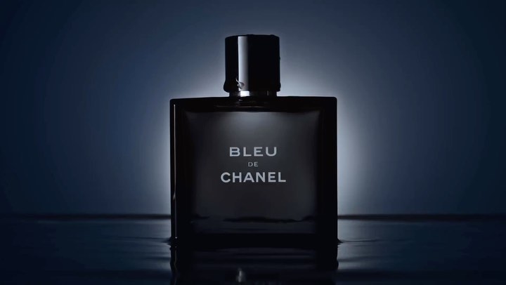 Close-up studio shot of a sleek, square Bleu de Chanel bottle with the brand name displayed against a gradient blue background.