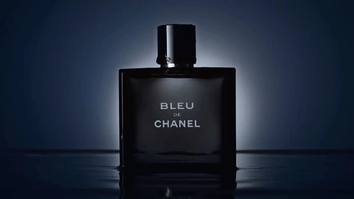 Close-up studio shot of a sleek, square Bleu de Chanel bottle with the brand name displayed against a gradient blue background.
