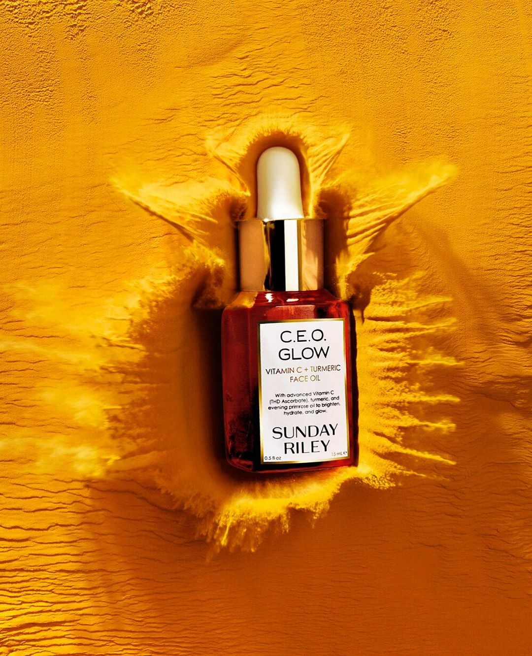 Close-up product shot of Sunday Riley C.E.O. Glow Vitamin C + Turmeric face oil against textured bright-yellow powder background.