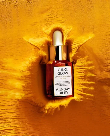 Close-up product shot of Sunday Riley C.E.O. Glow Vitamin C + Turmeric face oil against textured bright-yellow powder background.